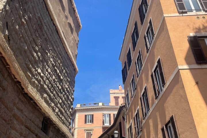 The huge ancient stone wall of the Forum of Augustus rising beside the ochre houses of Monti, seen from below against a blue sky