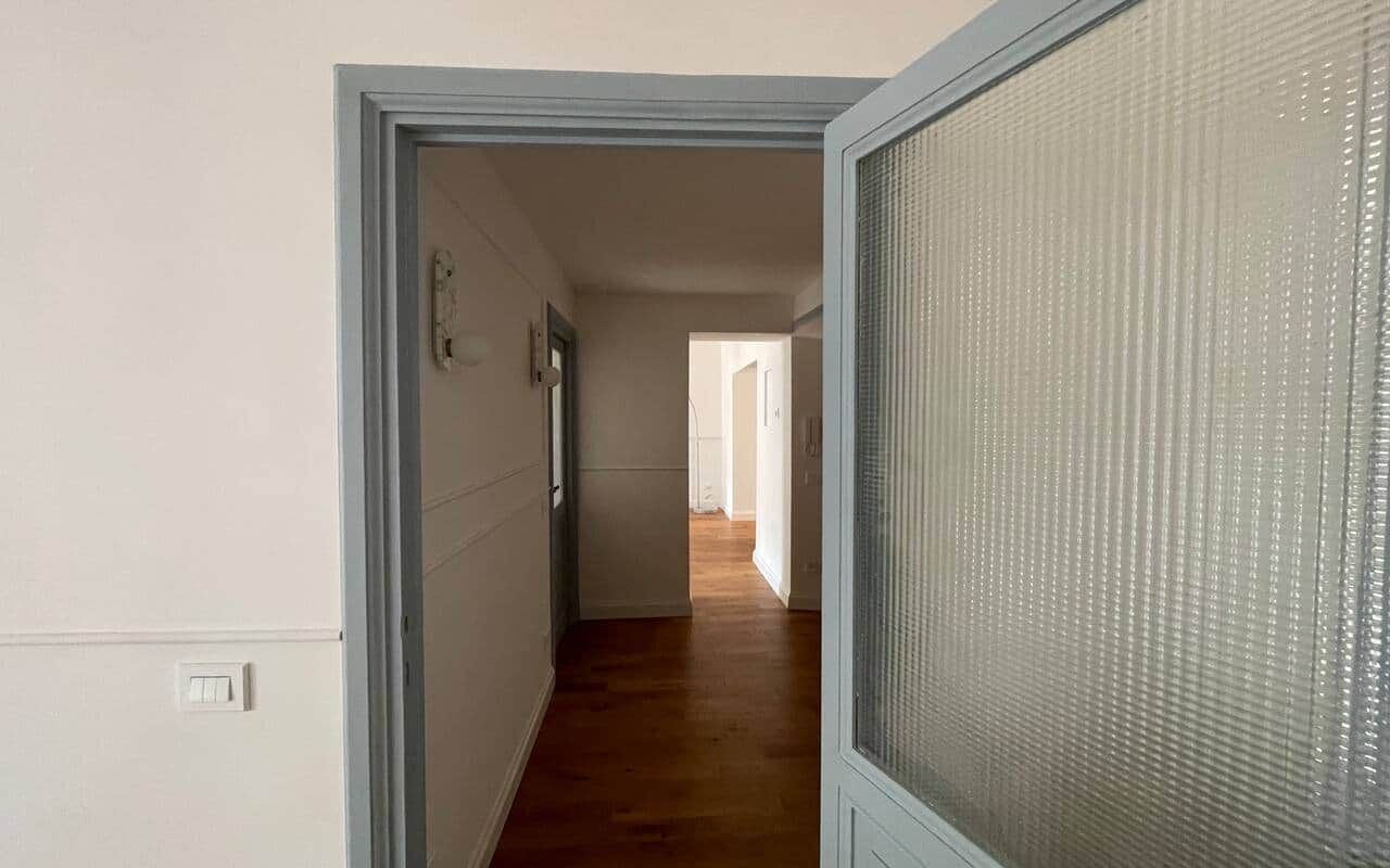 Hallway with dark oak floorboards running towards a lit room, framed by a grey-green door glazed with reeded glass