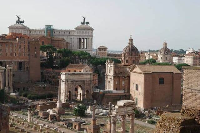 The Roman Forum seen across its ruins, with the Arch of Septimius Severus, church domes and the white marble of the Vittoriano behind